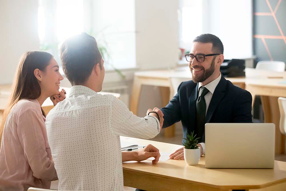 Advogado estendendo a mão apra cumprimentar clientes sorridentes, simbolizando a possibilidade de manter a clientela mesmo mudando o escritório de cidade