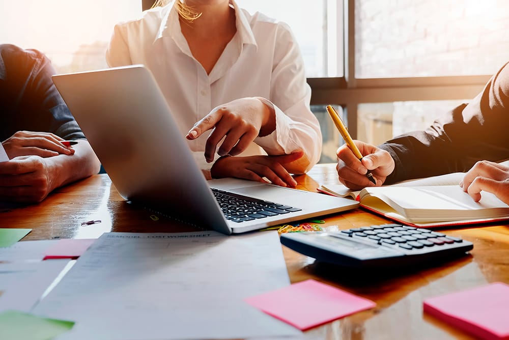 Alguns advogados em uma mesa em reunião apontando par aum notebook e com diversos documentos sobre a mesa, representando os cuidados para se ter um escritório de sucesso